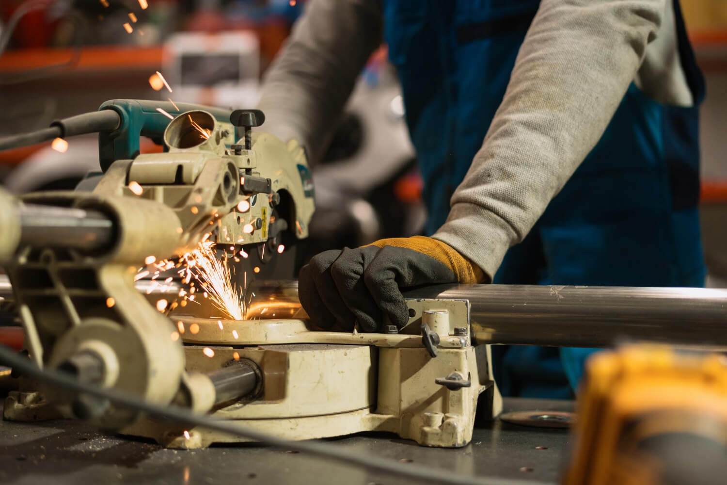 Worker wearing gloves cutting metal pipe with a circular saw, creating sparks.